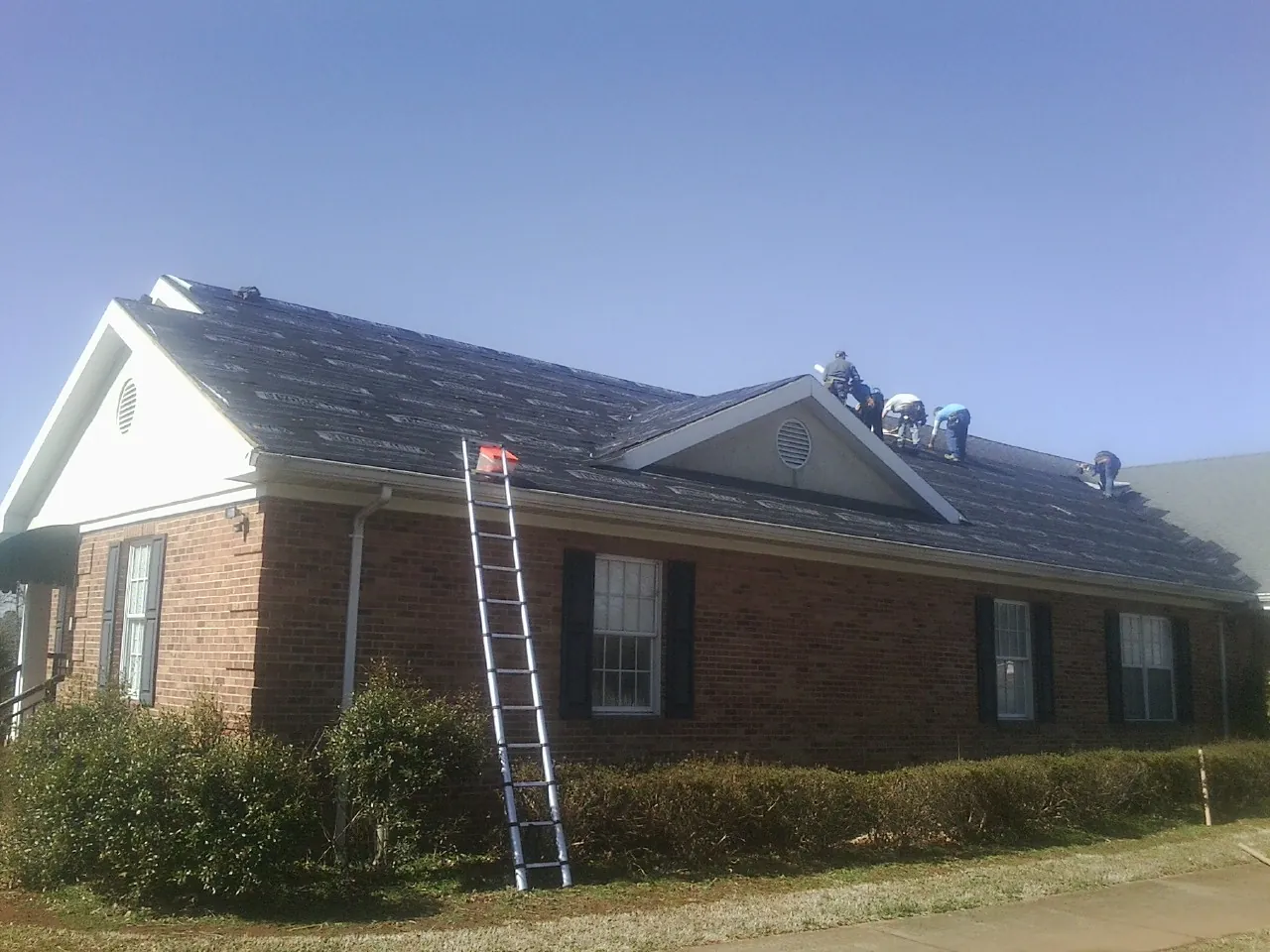 Crew tearing shingles off a brick ranch roof with a ladder set — Emergency Roof Repair work by our crew in Mount Prospect