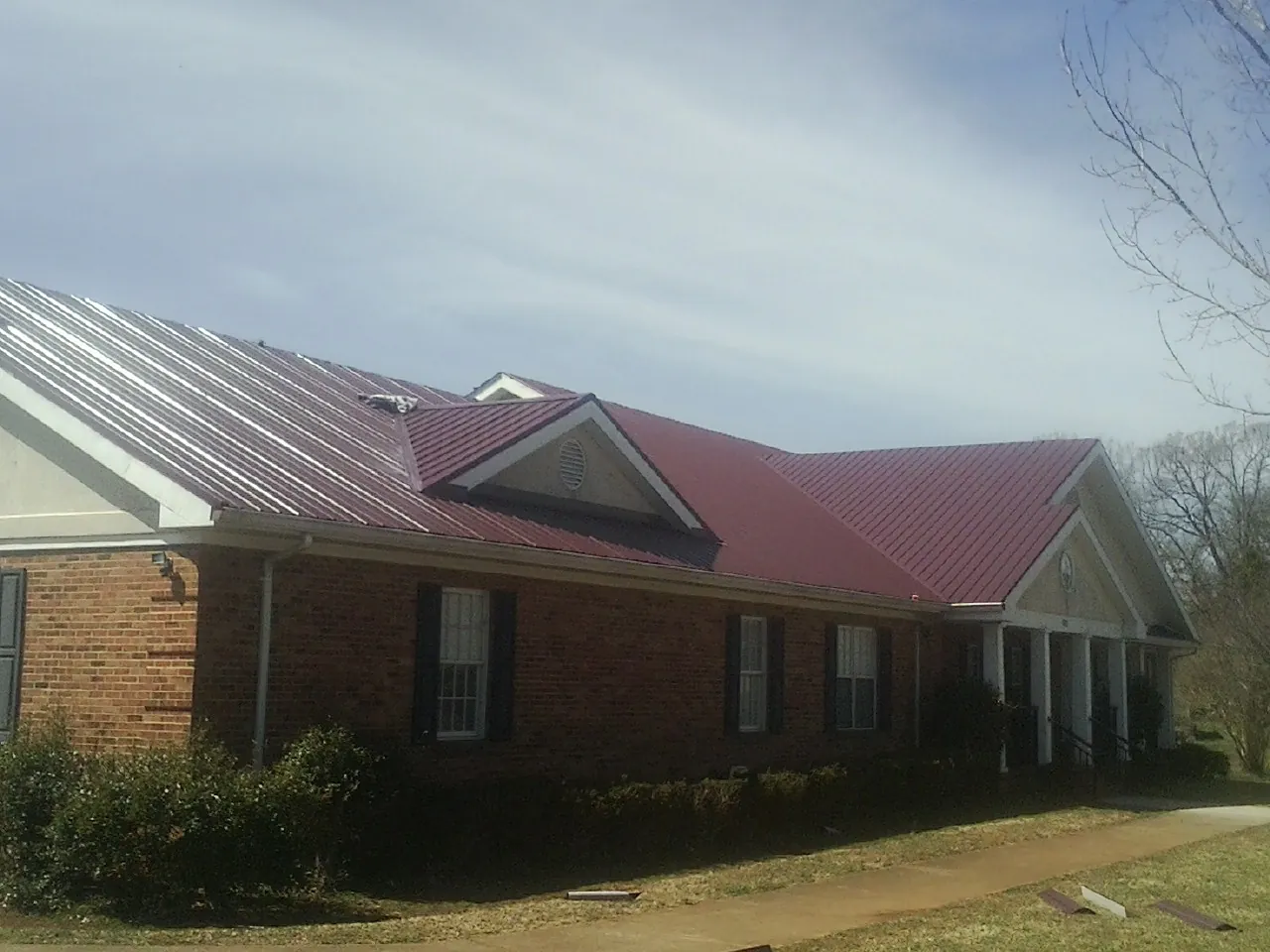 Red metal roof with gabled entries on a long brick building, from a Hail Damage Roof Repair job in Mount Prospect