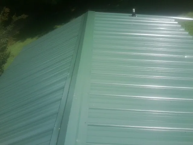 New green metal panels meeting at the ridge of a roof — Flat Roof Repair work by our crew in Mount Prospect