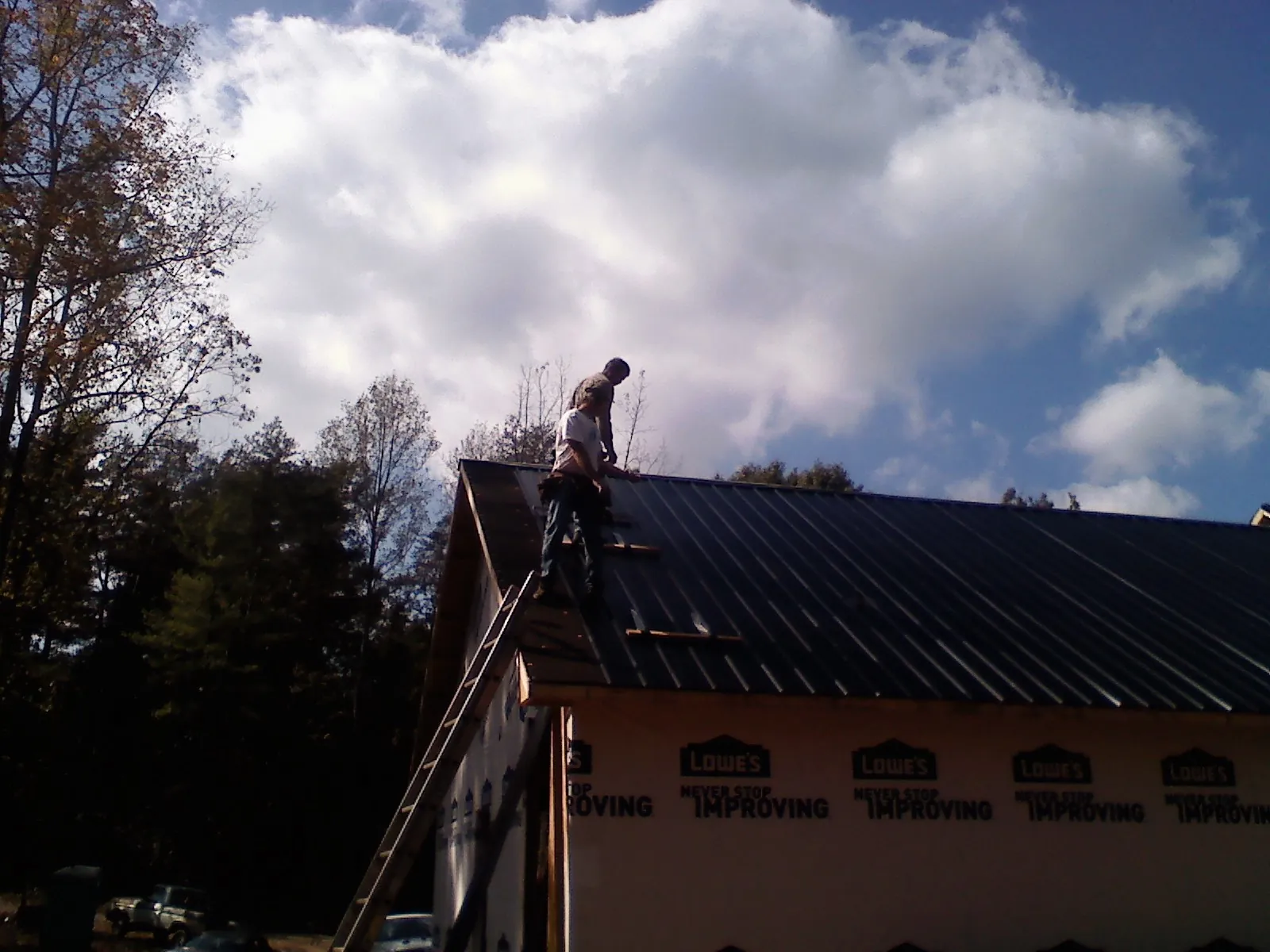 Roofer fastening dark metal panels high against a cloudy sky, from a Roof Inspection job in Mount Prospect